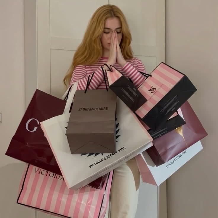 Someone holding an armful of shopping bags, hands together, eyes closed